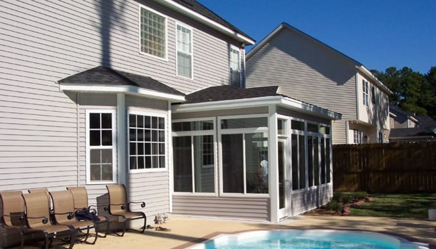 Muhler sunroom addition on a Lowcountry home White-frame Muhler sunroom addition on the back of a Lowcountry home beside a backyard pool