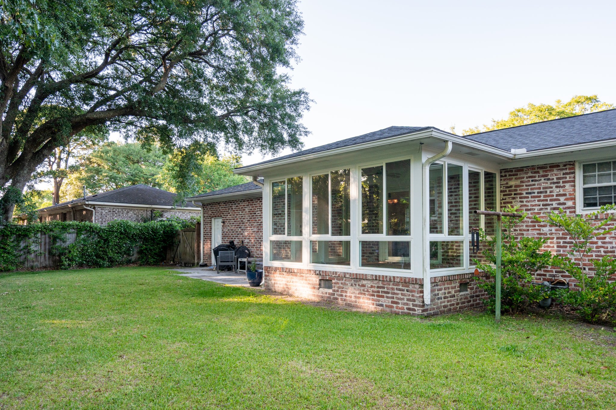 The finished room at the rear corner of a brick ranch, white frames on a brick knee wall, mature trees behind.
